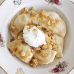 a plate with several pierogi in a decorated plate with caramelized onions and sour cream