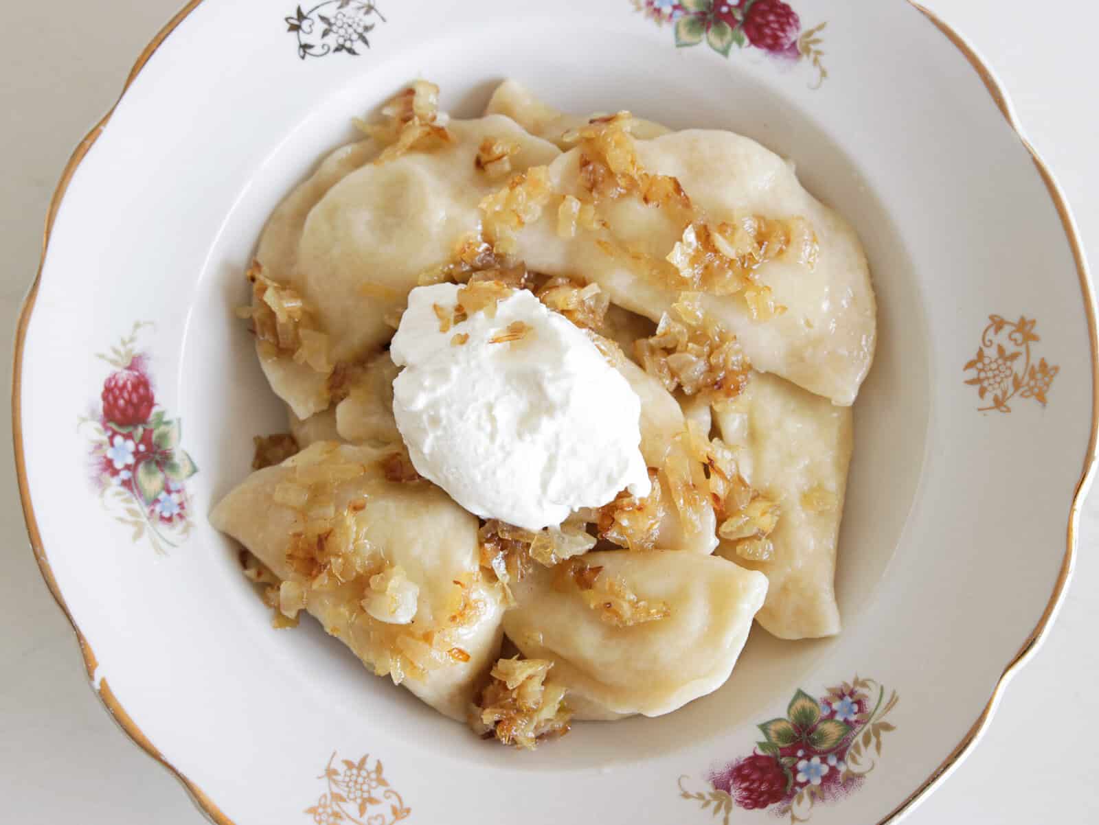 a plate with several pierogi in a decorated plate with caramelized onions and sour cream