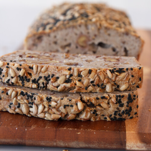 two slices of buckwheat bread on a cutting board and the rest of the loaf is in the background