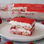 a vibrant strawberry tiramisu on a plate served with fresh strawberries and topped with strawberry powder