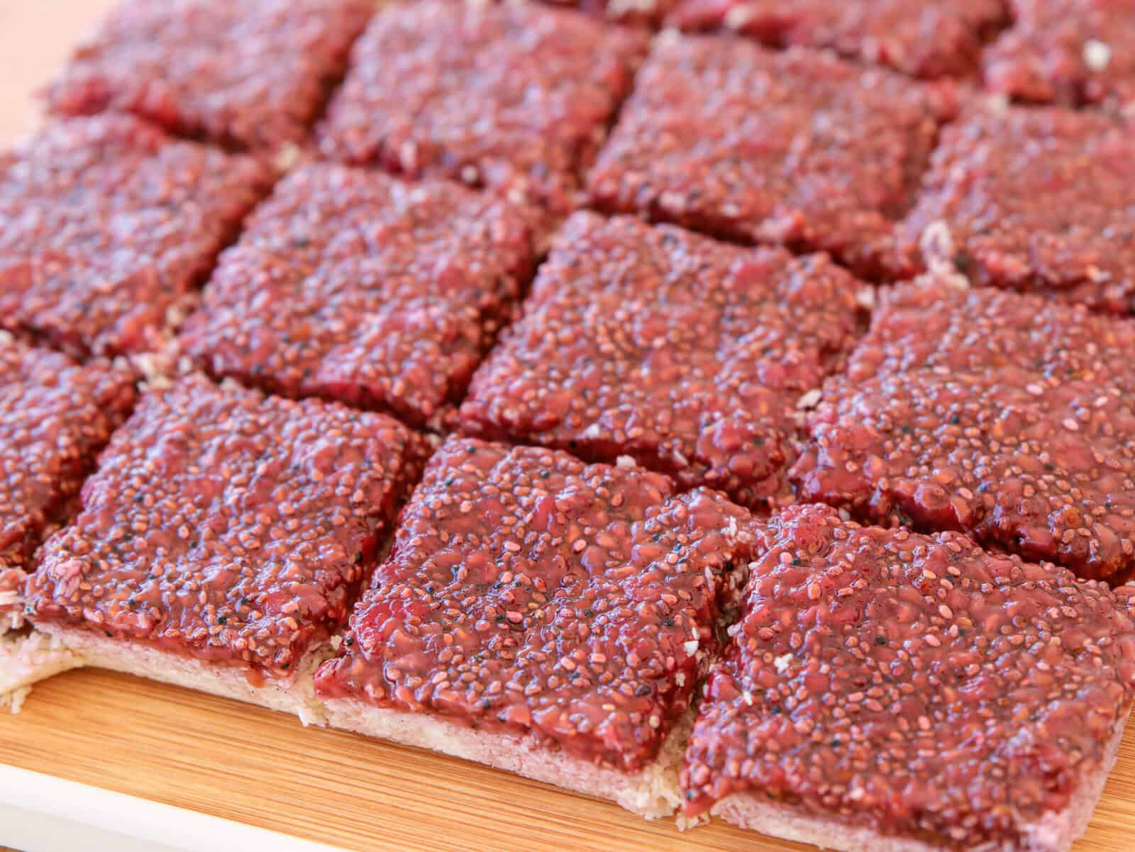 Close-up of several square raspberry chia seed bars arranged neatly on a wooden surface, showing their textured, red, seed-studded tops and lightly colored base.