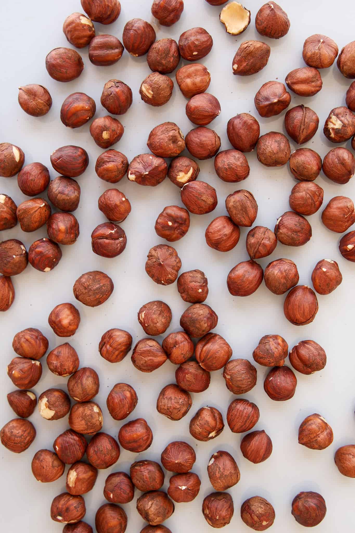 A scattered arrangement of whole hazelnuts with brown shells on a light, neutral background.