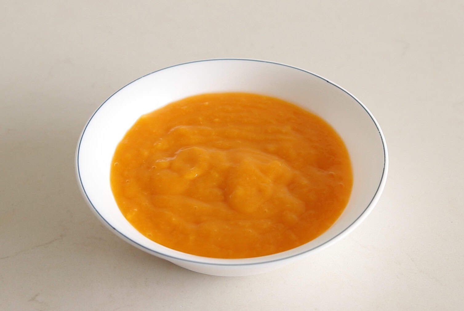 A white bowl filled with smooth orange puree, placed on a light-colored surface.