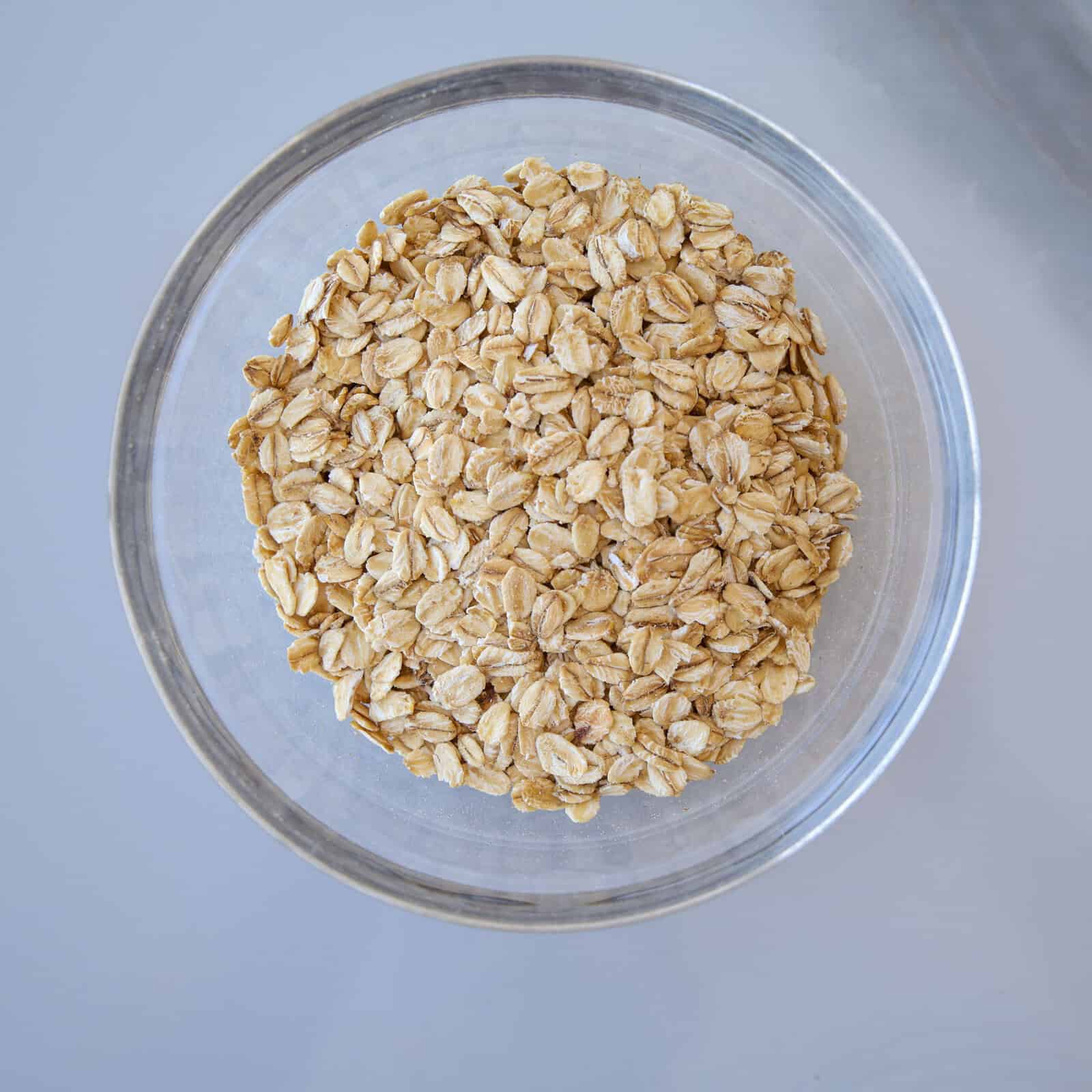 A clear glass bowl filled with rolled oats, viewed from above, on a light gray surface.