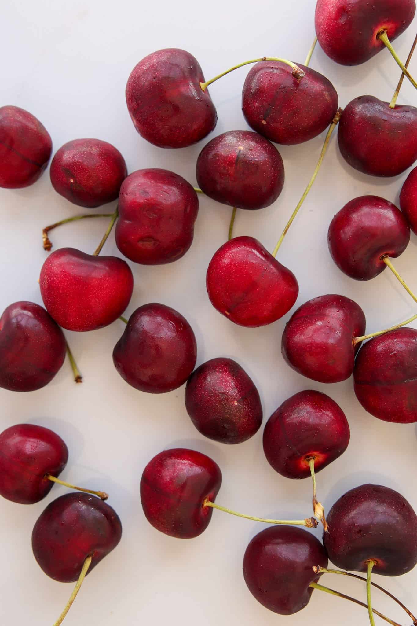Scattered fresh red cherries with green stems on a light, white background.