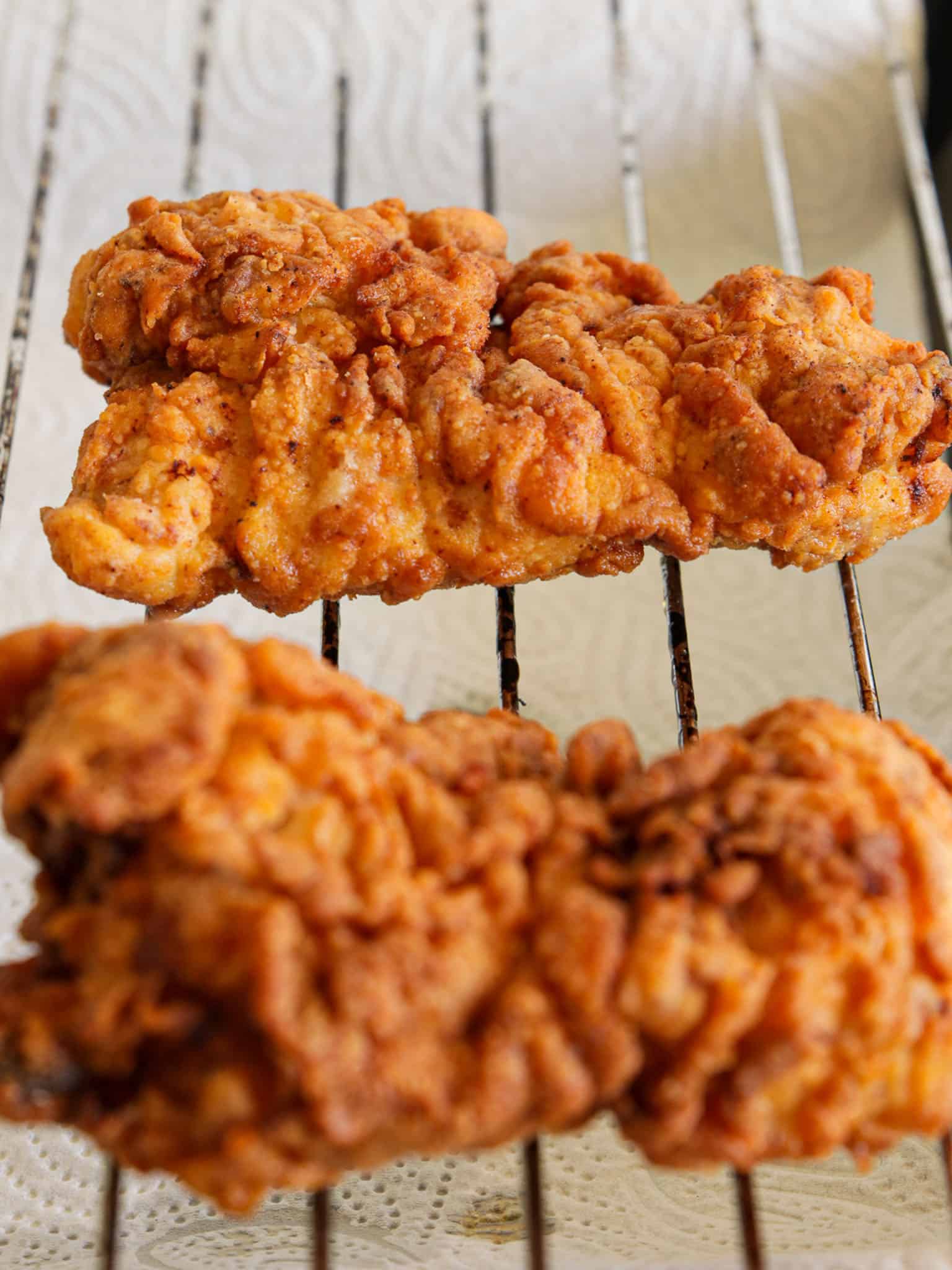 Two pieces of golden, crispy fried chicken resting on a wire rack with white paper towels underneath to absorb excess oil.