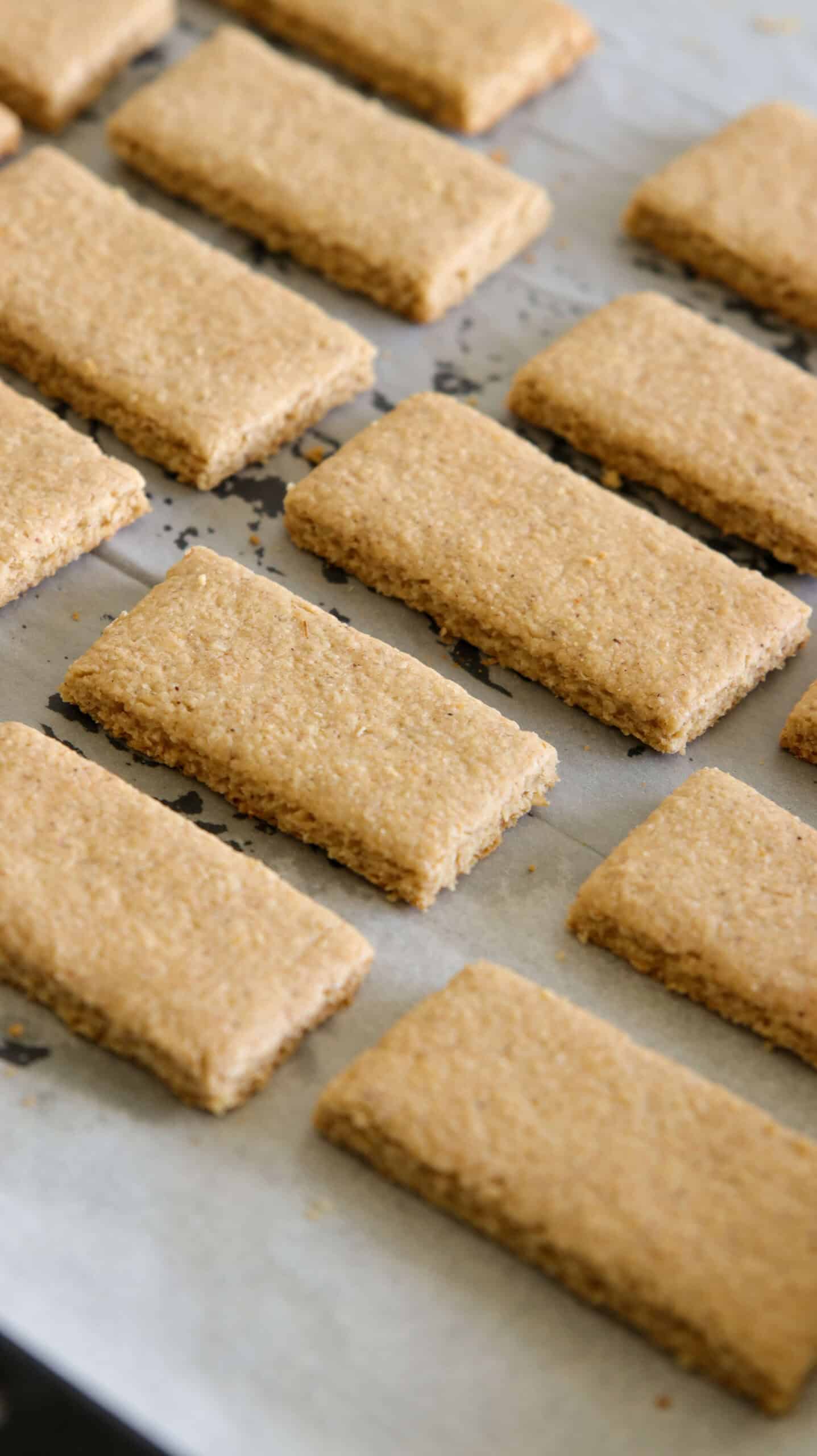Rectangular, golden-brown homemade graham crackers arranged in neat rows on parchment paper, cooling after baking.