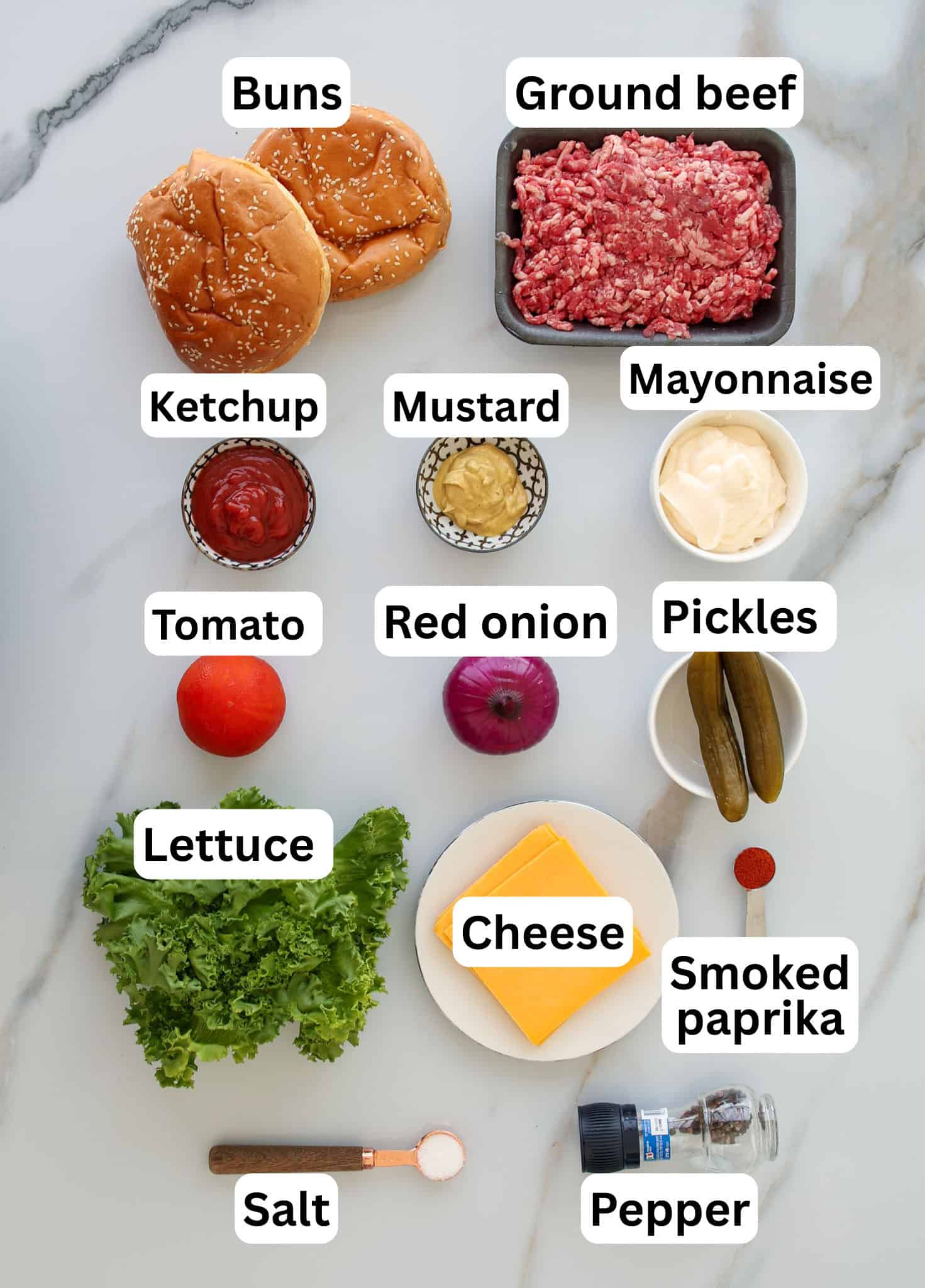 Top-down view of labeled burger ingredients on a white surface, including buns, ground beef, ketchup, mustard, mayonnaise, tomato, red onion, pickles, lettuce, cheese, smoked paprika, salt, and pepper.