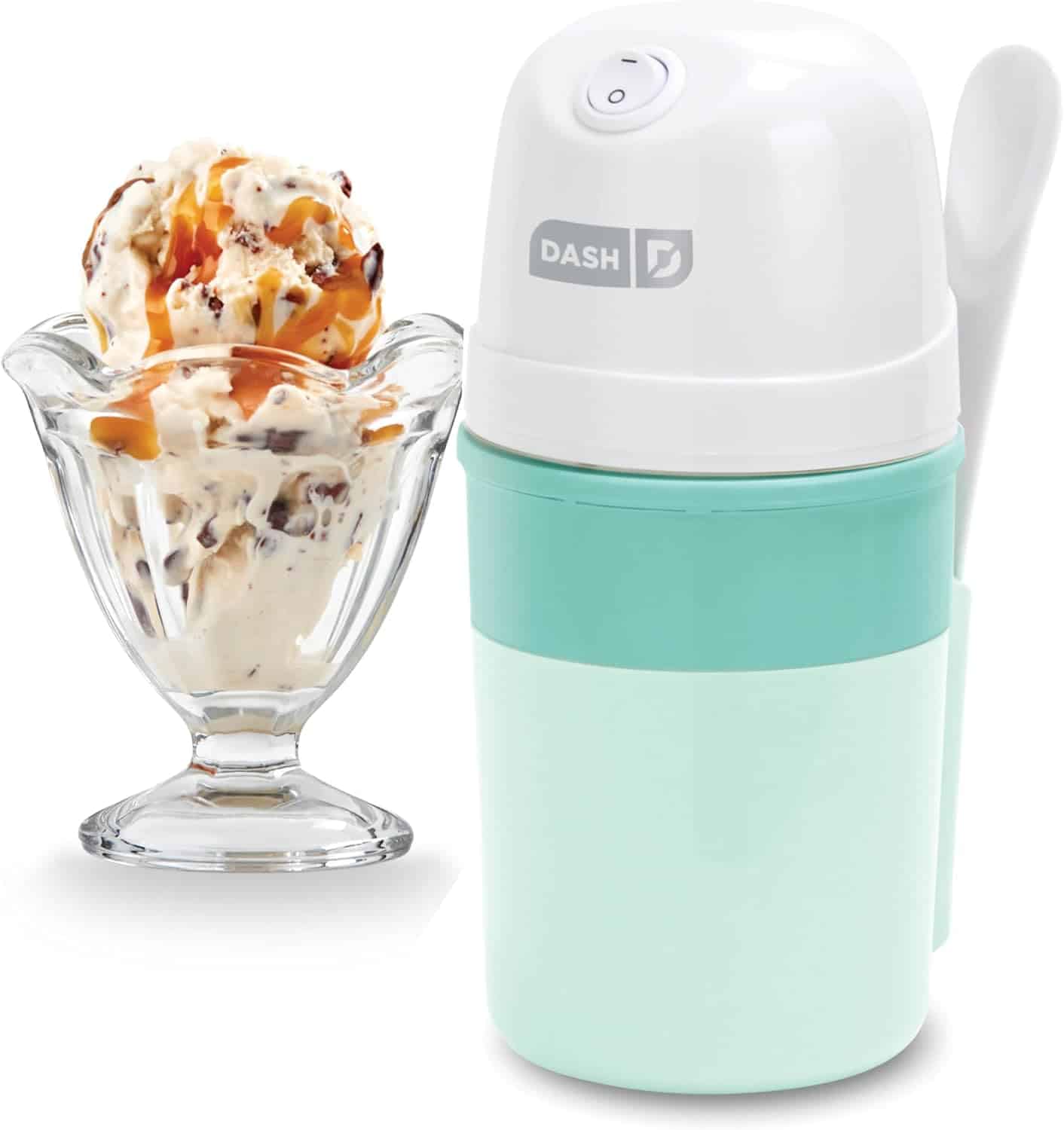 A mint green and white Dash ice cream maker sits next to a glass dish filled with vanilla ice cream topped with caramel sauce. A white spoon is attached to the ice cream maker.