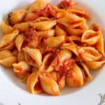 A plate of shell-shaped pasta topped with tomato sauce, served on a white dish with a decorative border.