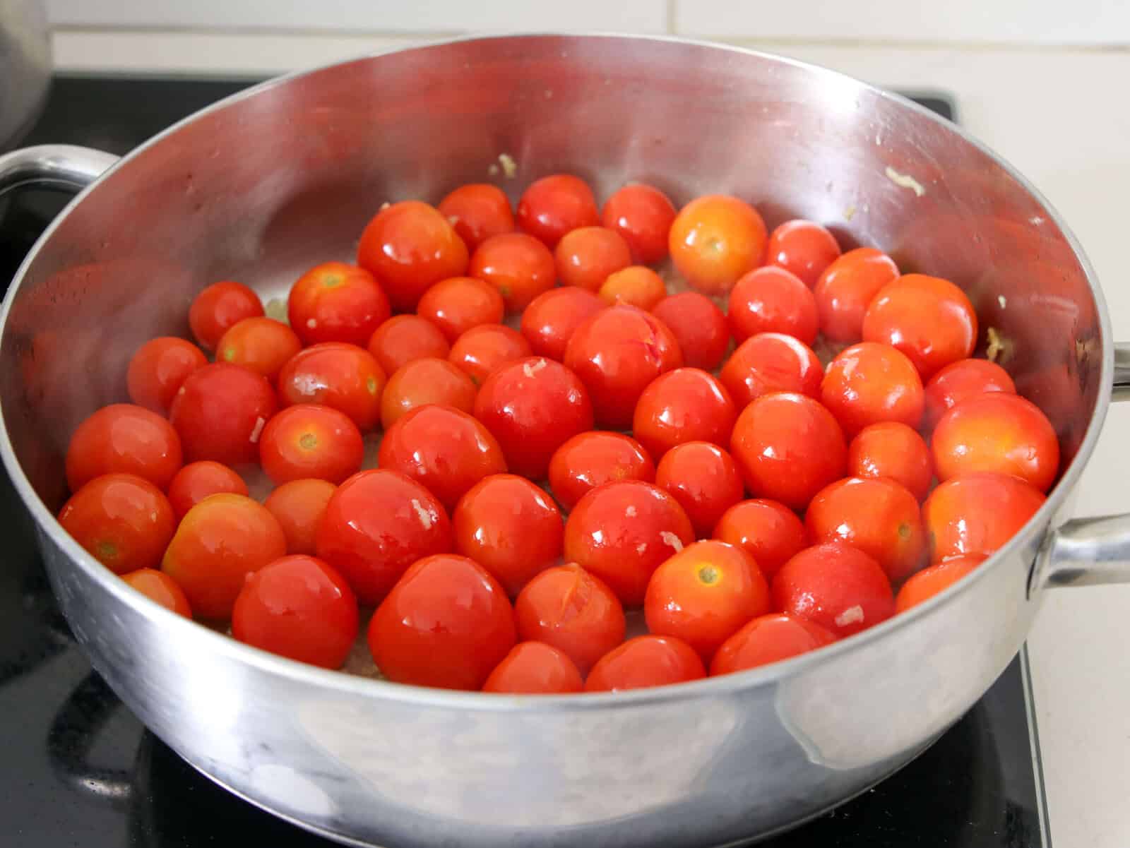 A large silver pan filled with fresh, whole cherry tomatoes is placed on a stovetop, ready to be cooked.