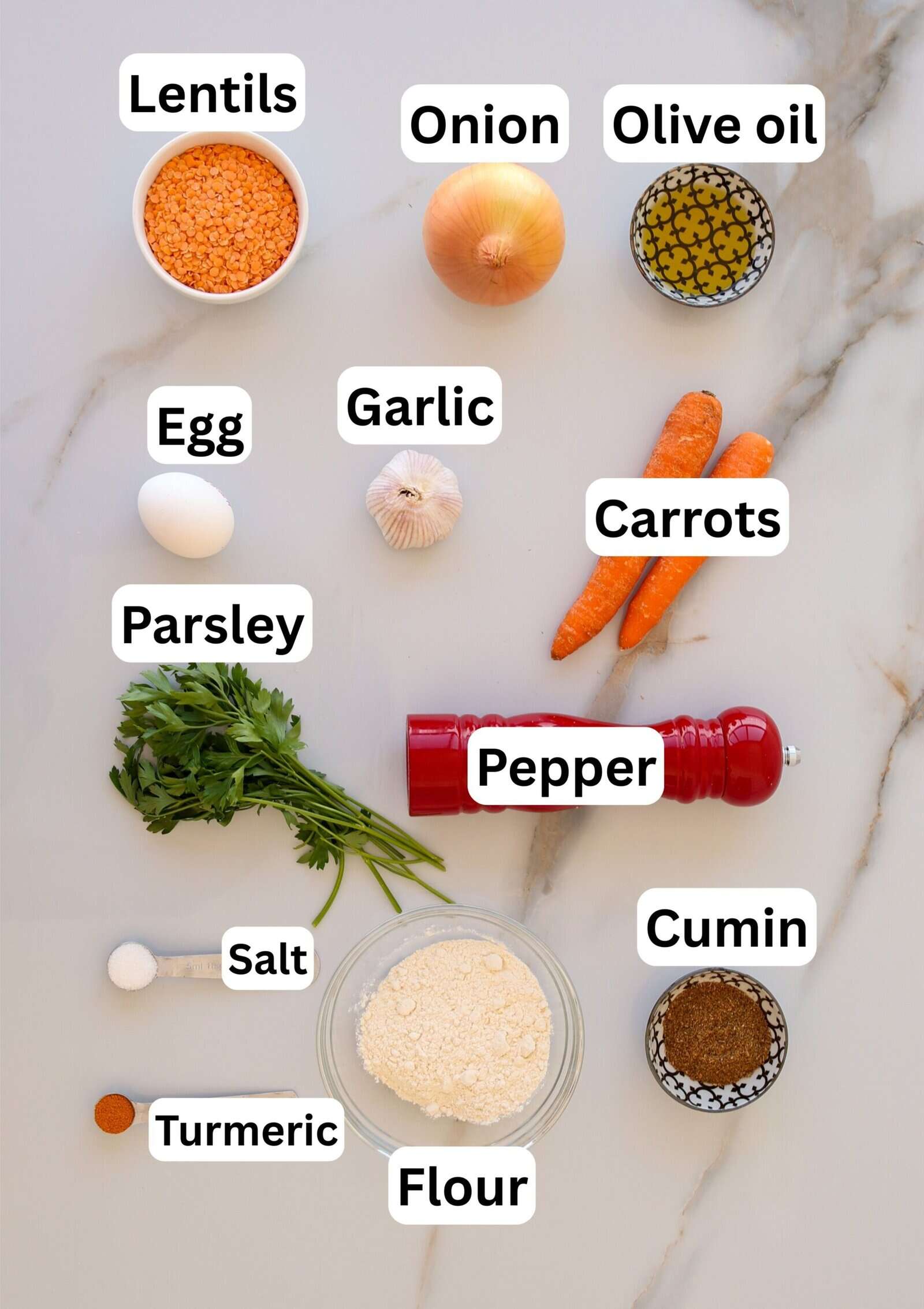 A flat lay of labeled ingredients on a marble surface: lentils, onion, olive oil, egg, garlic, carrots, parsley, pepper, salt, cumin, turmeric, and flour.