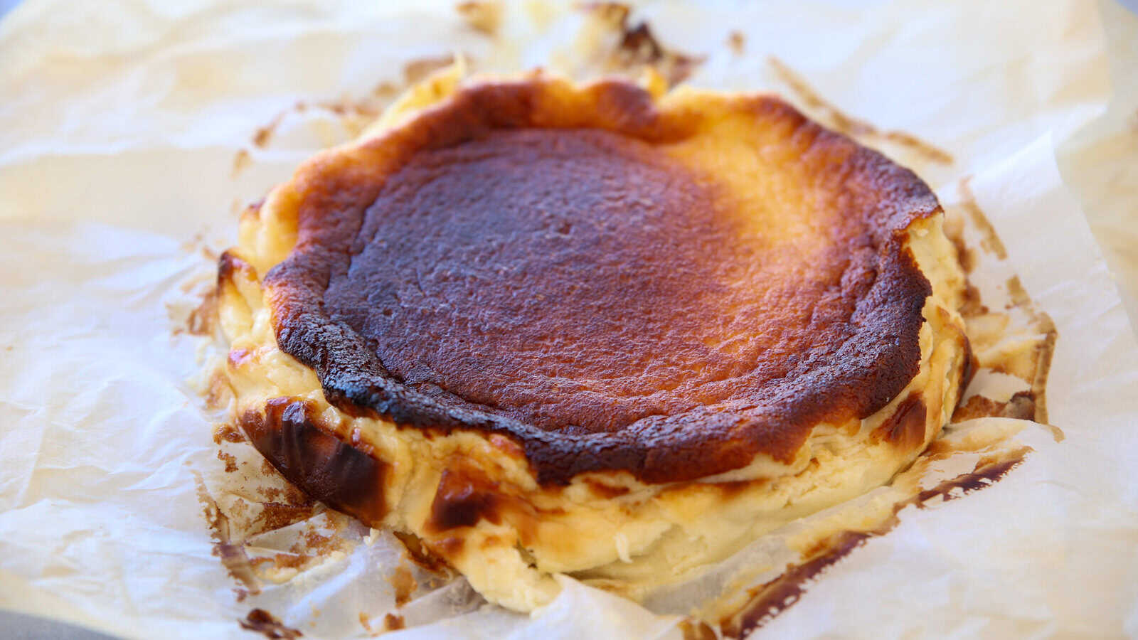 Classic Basque Cheesecake Recipe (Easy & Creamy!) A Basque burnt cheesecake with a dark, caramelized top sits on crumpled parchment paper, showing its creamy, slightly cracked edges and rustic appearance.