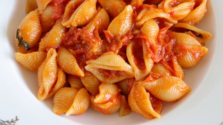 A close-up of conchiglie pasta shells covered in a chunky cherry tomato sauce, served on a white plate.