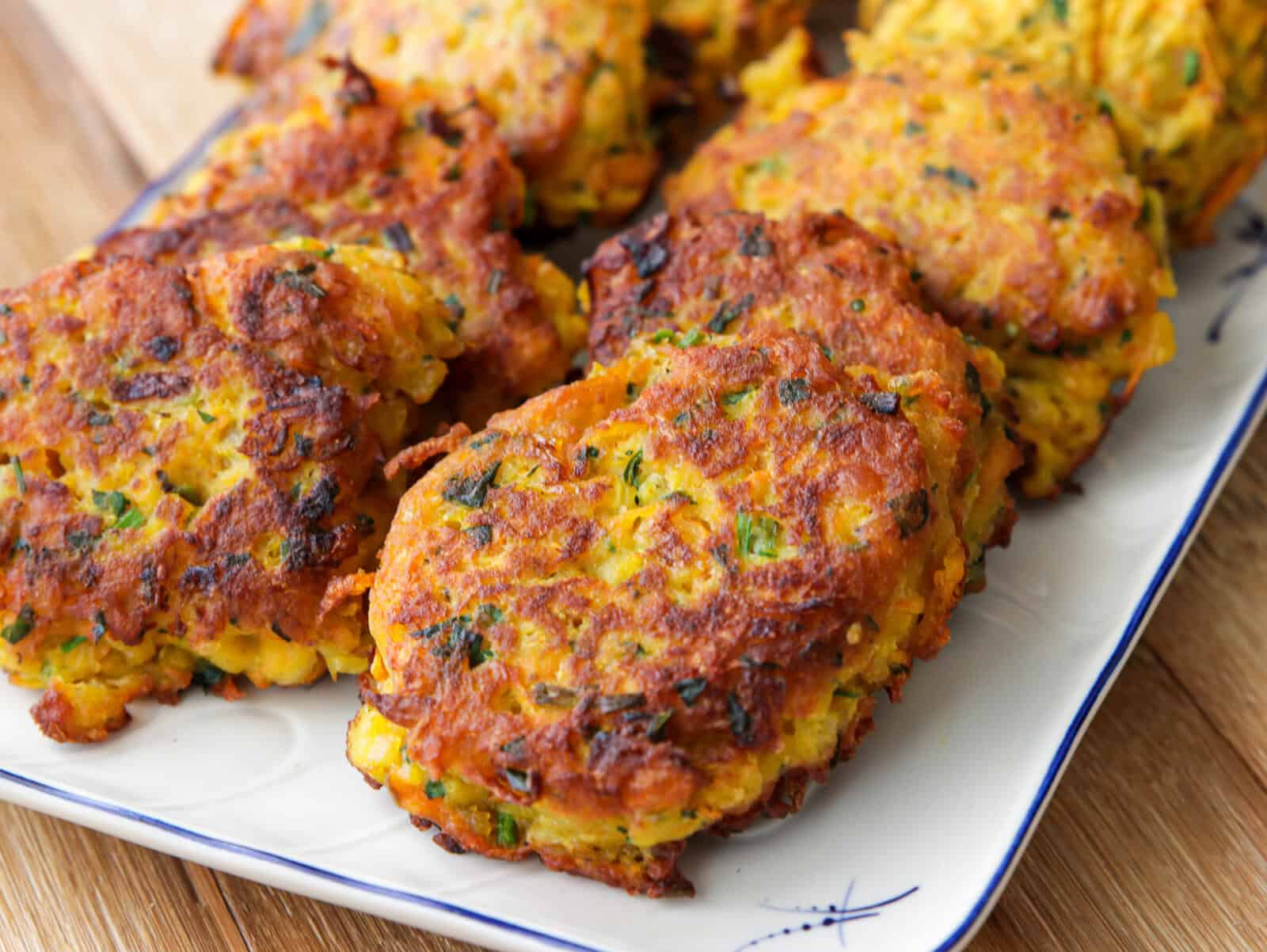 Golden-brown red lentil fritters with visible herbs, arranged on a white rectangular plate with blue accents, sitting on a wooden surface.