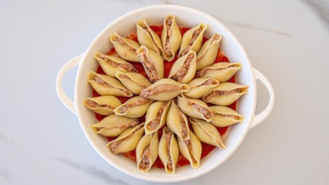 Cheesy Beef Stuffed Pasta Shells A white oval dish filled with large pasta shells stuffed with meat filling, arranged in a circular pattern over a layer of red tomato sauce.