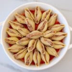 A round white dish filled with large pasta shells stuffed with a meat mixture, arranged in a circular pattern over a layer of tomato sauce.