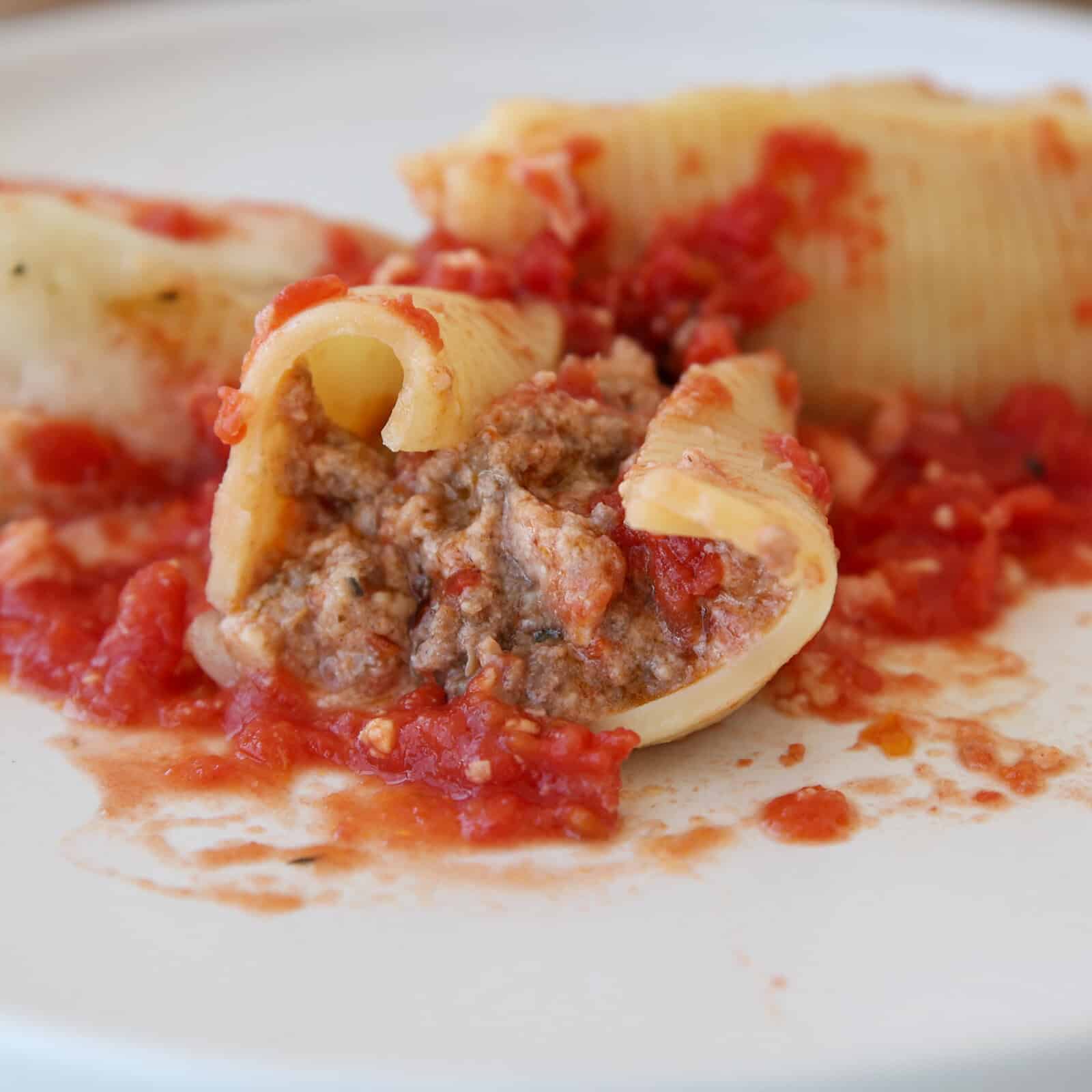 Close-up of pasta shells stuffed with ground meat and cheese, topped with chunky tomato sauce, served on a white plate.