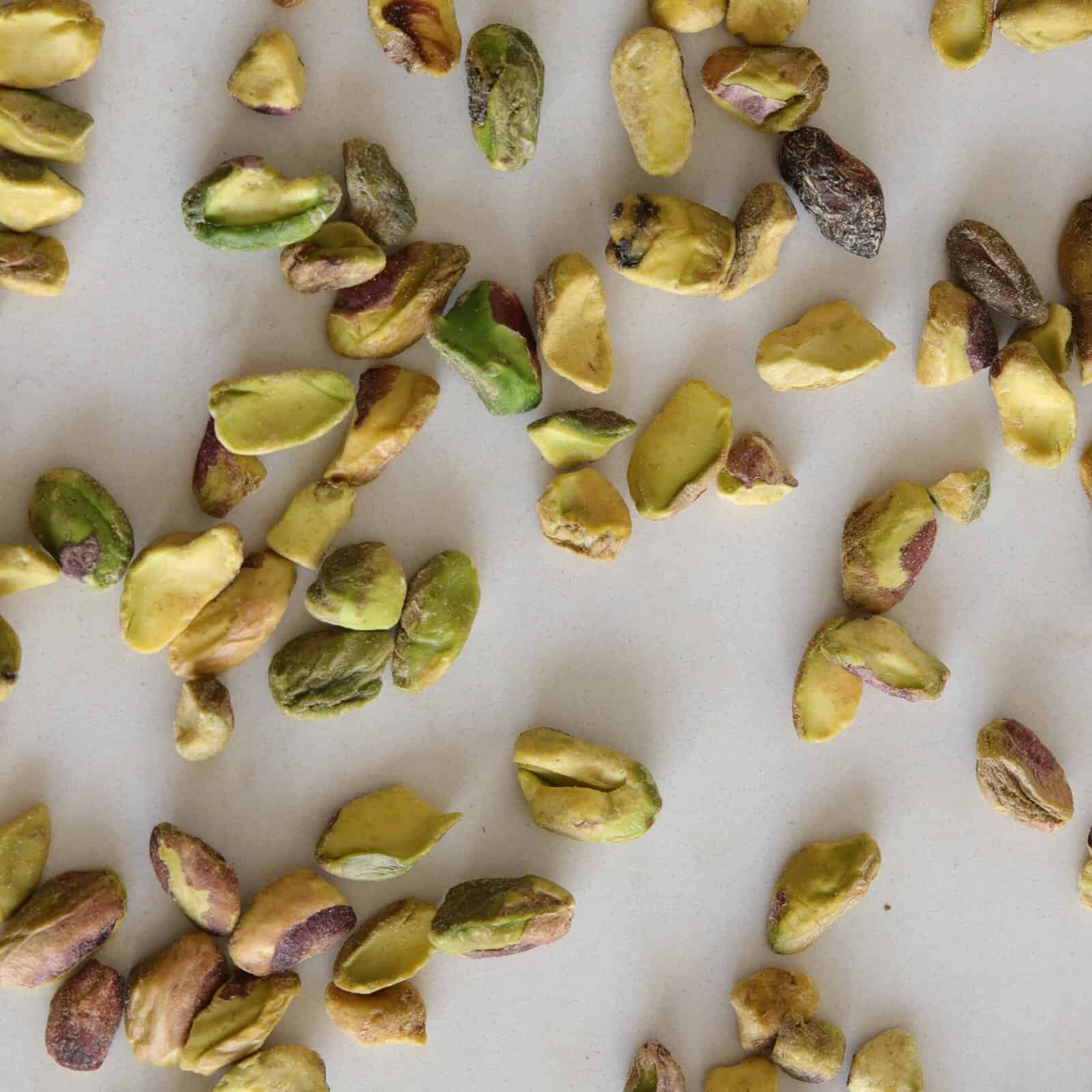 Shelled pistachio nuts, some whole and some broken, scattered on a light-colored surface.