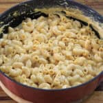 A pot filled with creamy macaroni and cheese sits on a wooden surface. The pasta is coated in a thick, melted cheese sauce and looks freshly prepared.