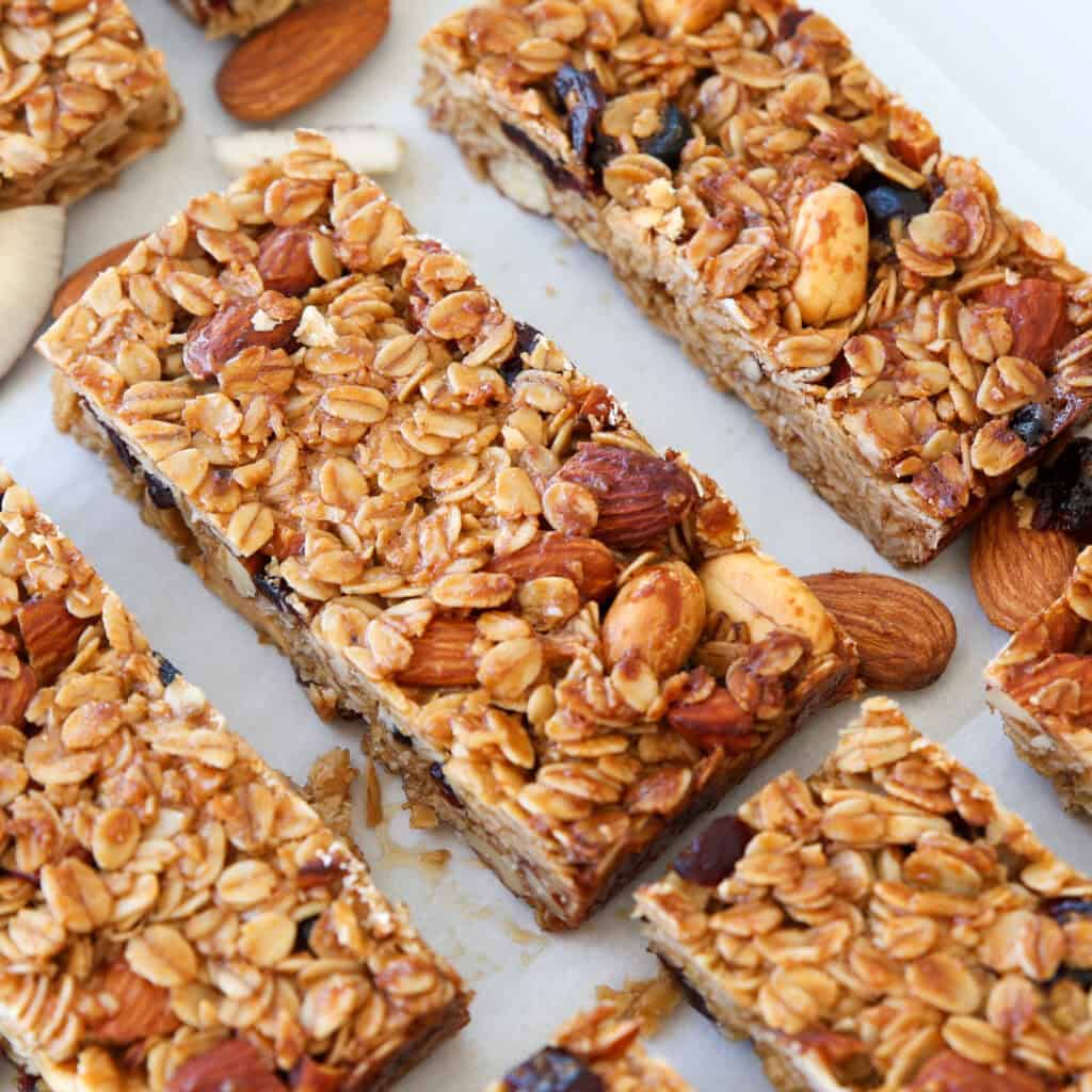Close-up of homemade granola bars containing oats, whole almonds, and dried fruit, arranged on parchment paper with a few loose almonds scattered around.