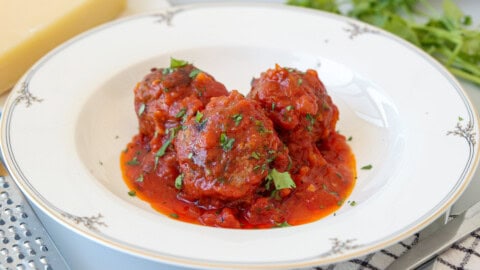Best Italian Meatballs in Tomato Sauce | Easy and Juicy Three meatballs covered in tomato sauce, garnished with chopped parsley, served on a white decorative plate.