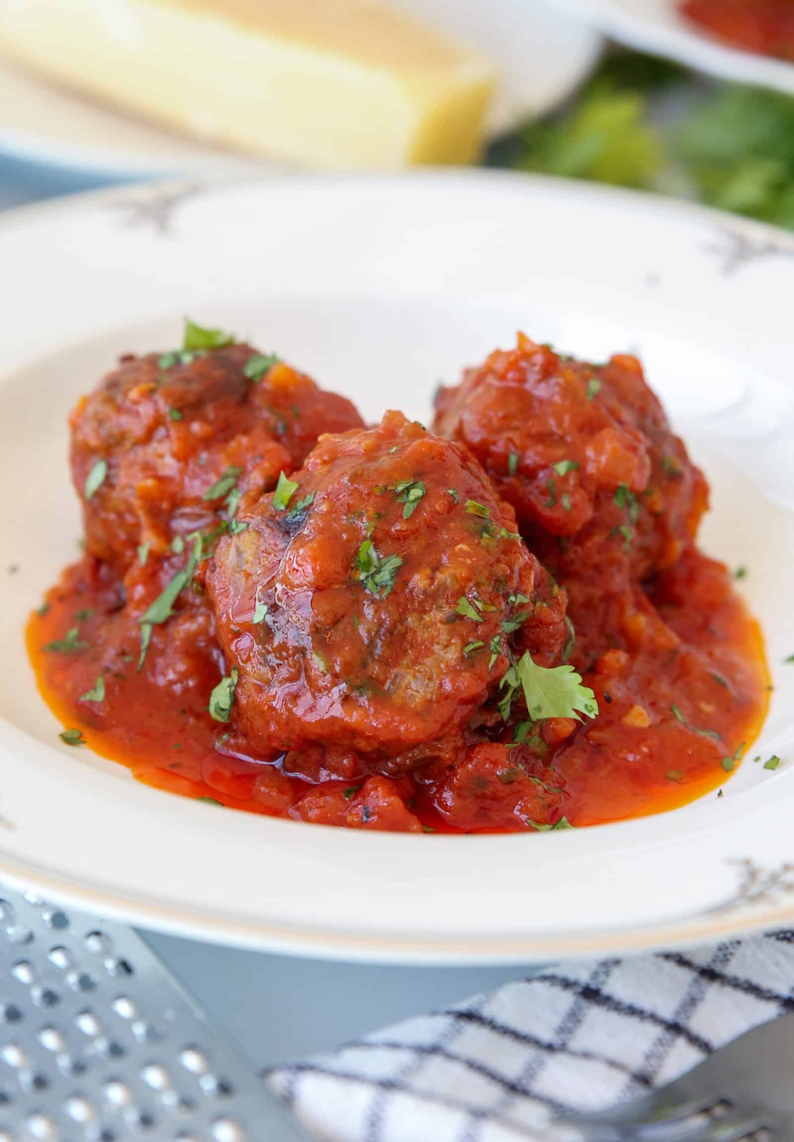 Three meatballs topped with tomato sauce and garnished with chopped parsley are served on a white plate.