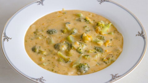 Easy Broccoli Cheddar Soup (Panera Copycat) A white bowl with decorative trim filled with creamy broccoli cheddar soup, featuring chunks of broccoli and melted cheese in a thick, orange-tinted broth.