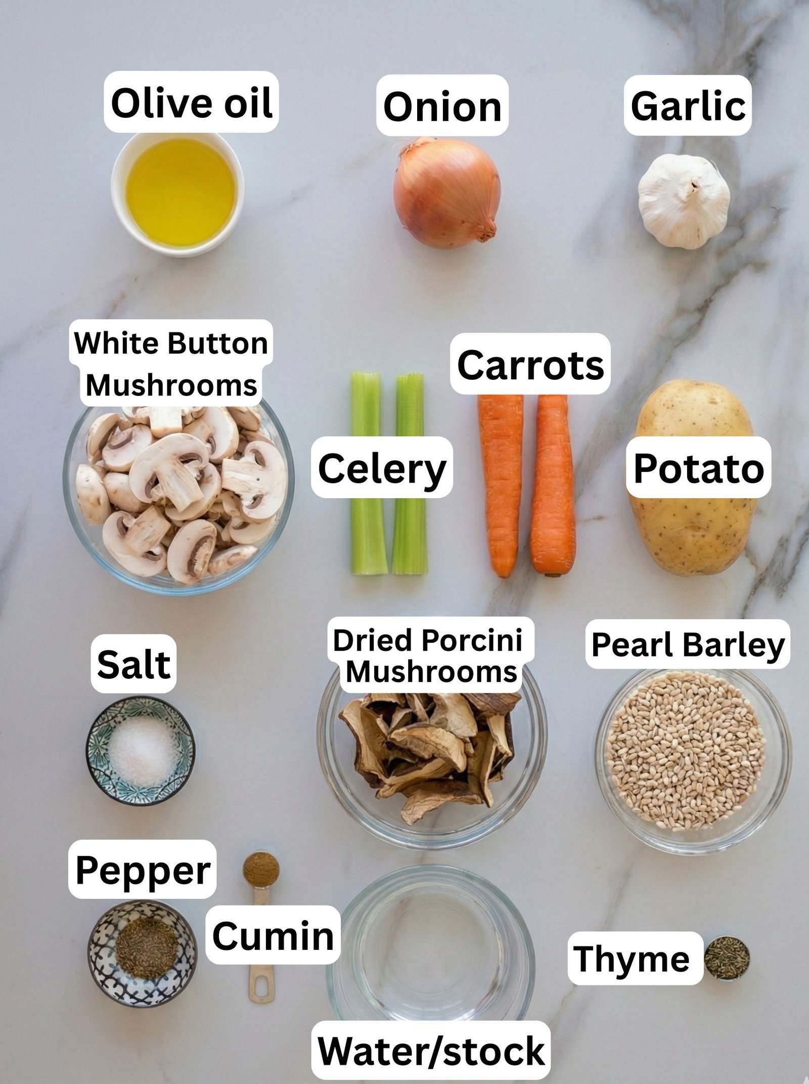 Ingredients for a soup are arranged on a white surface and labeled: olive oil, onion, garlic, white button mushrooms, celery, carrots, potato, salt, pepper, cumin, dried porcini mushrooms, water/stock, pearl barley, and thyme.
