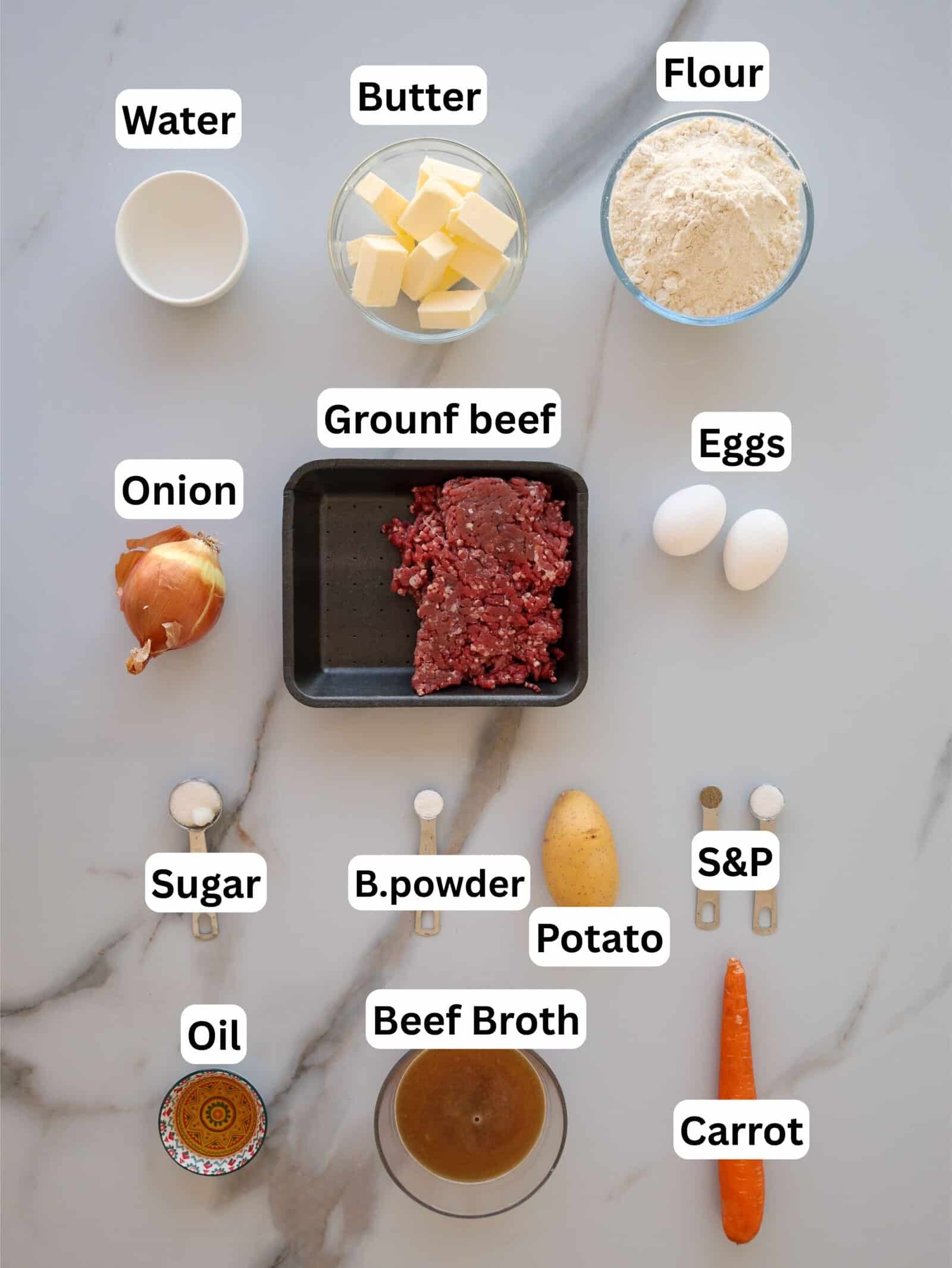 Nine labeled ingredients on a marble surface: water, butter, flour, ground beef, eggs, onion, sugar, baking powder, potato, oil, beef broth, salt and pepper, and a carrot. Each ingredient is in a separate container.