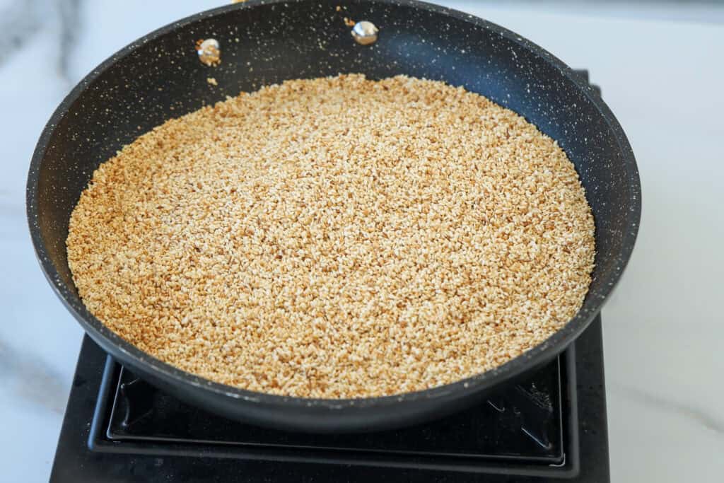 A large nonstick skillet filled with toasted sesame seeds sits on a stovetop.