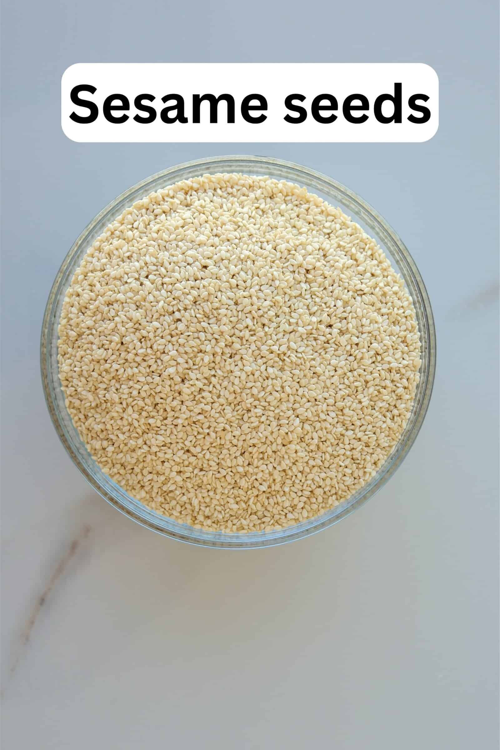 A glass bowl filled with sesame seeds sits on a light-colored surface. The words "Sesame seeds" appear above the bowl in bold text.