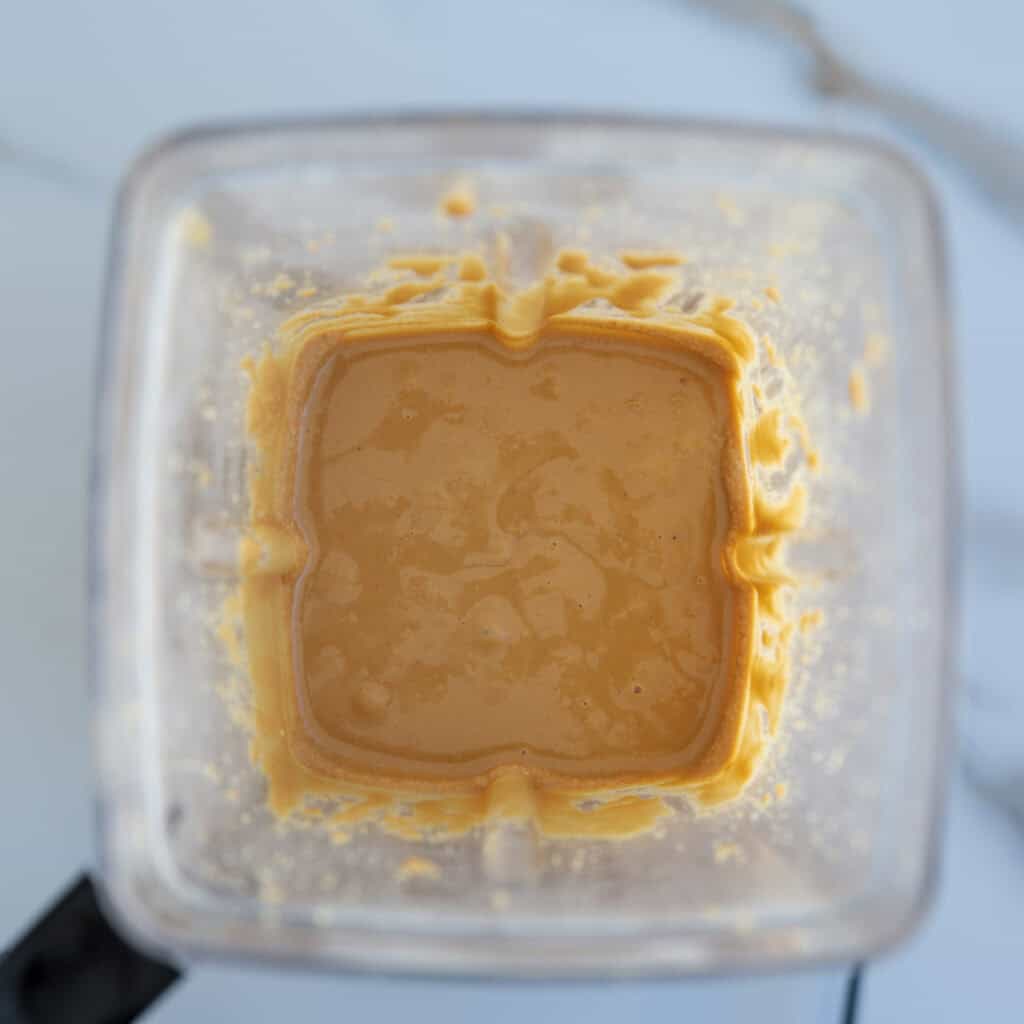 Top-down view of a blender containing a smooth, light orange mixture with some residue on the sides, sitting on a white surface.