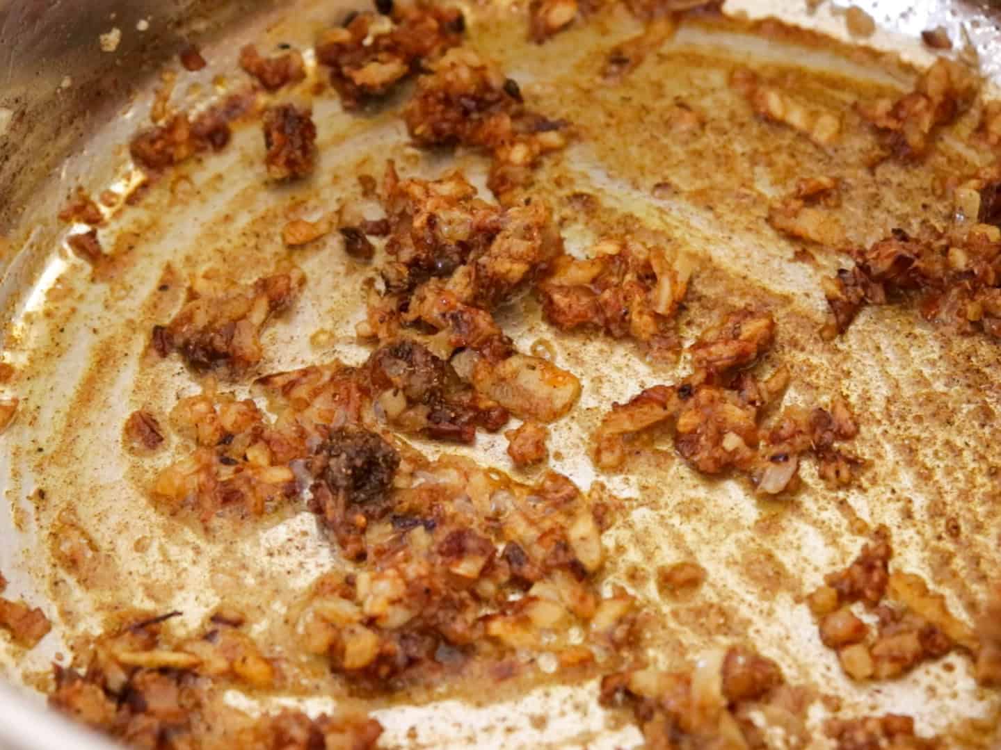 Chopped onions are browned and caramelized in a pan, with bits sticking to the bottom and a light coating of oil.