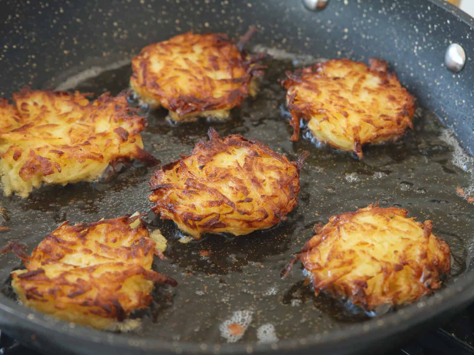 Golden brown potato latkes sizzling in hot oil in a frying pan.