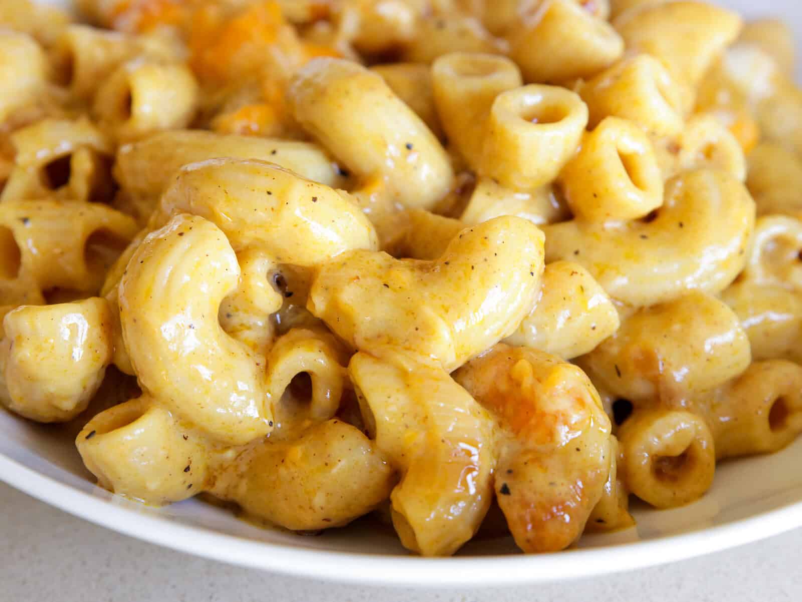 Close-up of creamy curry mac and cheese in a white bowl, with golden cheesy sauce coating the curved pasta and visible browned bits throughout.
