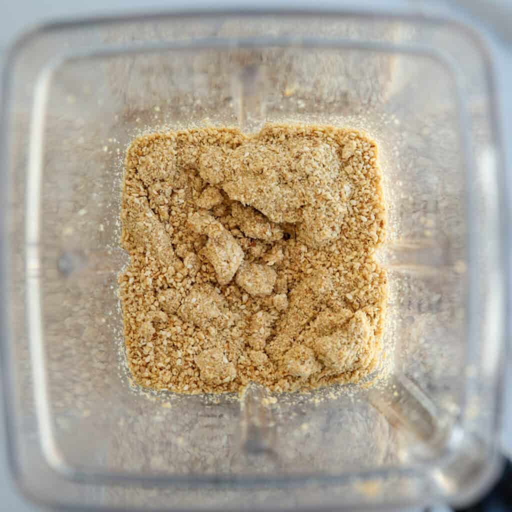 Crushed graham crackers or cookies in a blender, viewed from above, showing a coarse, crumbly texture.