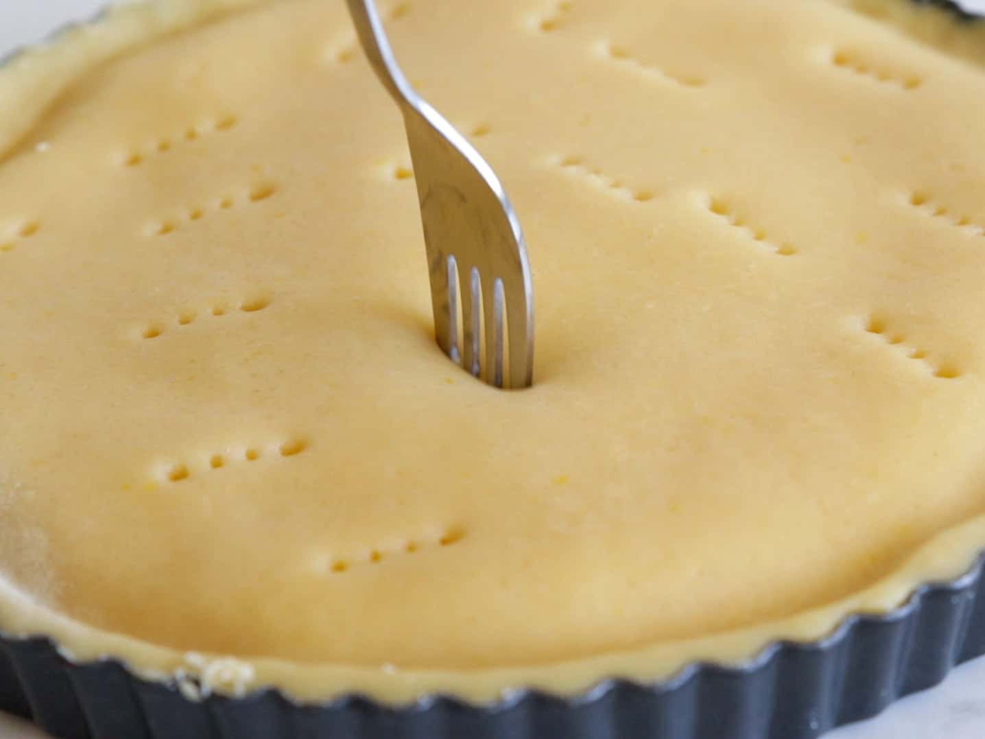 A close-up of a pie crust in a tart pan being pricked with a fork to create small holes before baking.