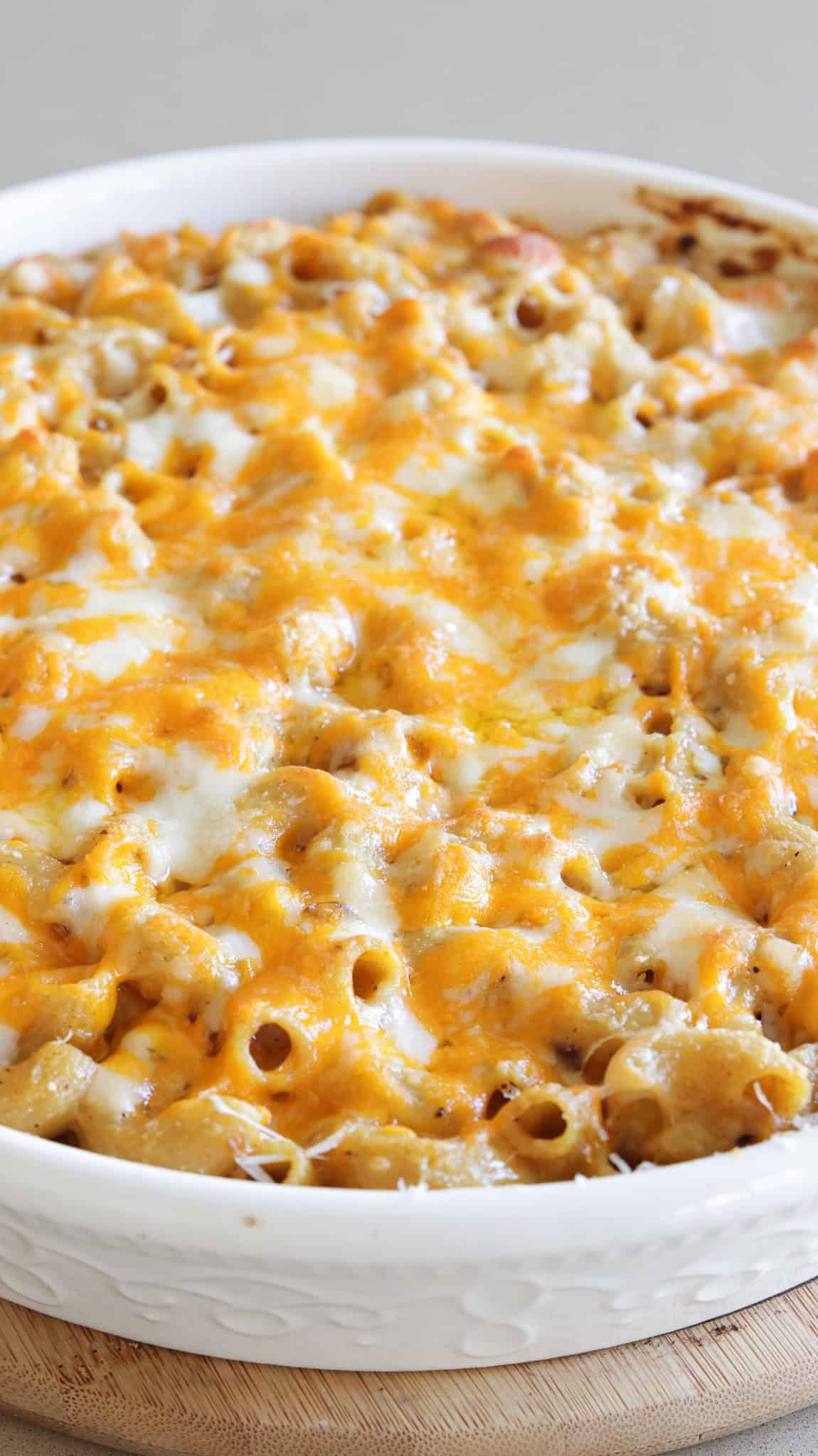 A close-up of a baked casserole dish filled with curry macaroni and cheese, topped with a layer of melted golden cheddar and mozzarella cheese. The dish sits on a light wooden surface.