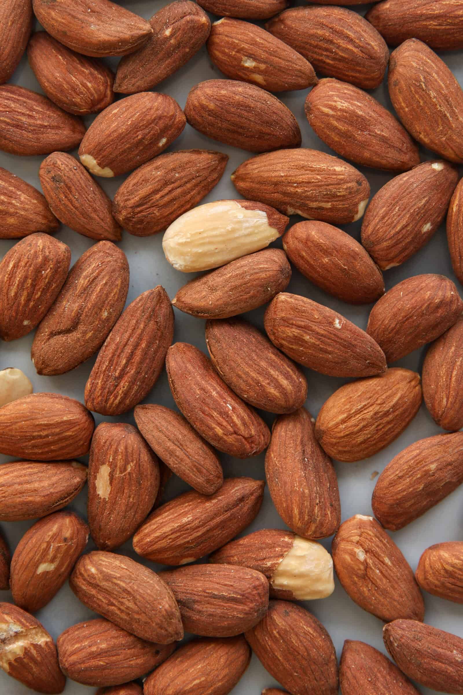 A close-up view of several unpeeled almonds scattered on a surface, with a few peeled almonds standing out among the brown ones.