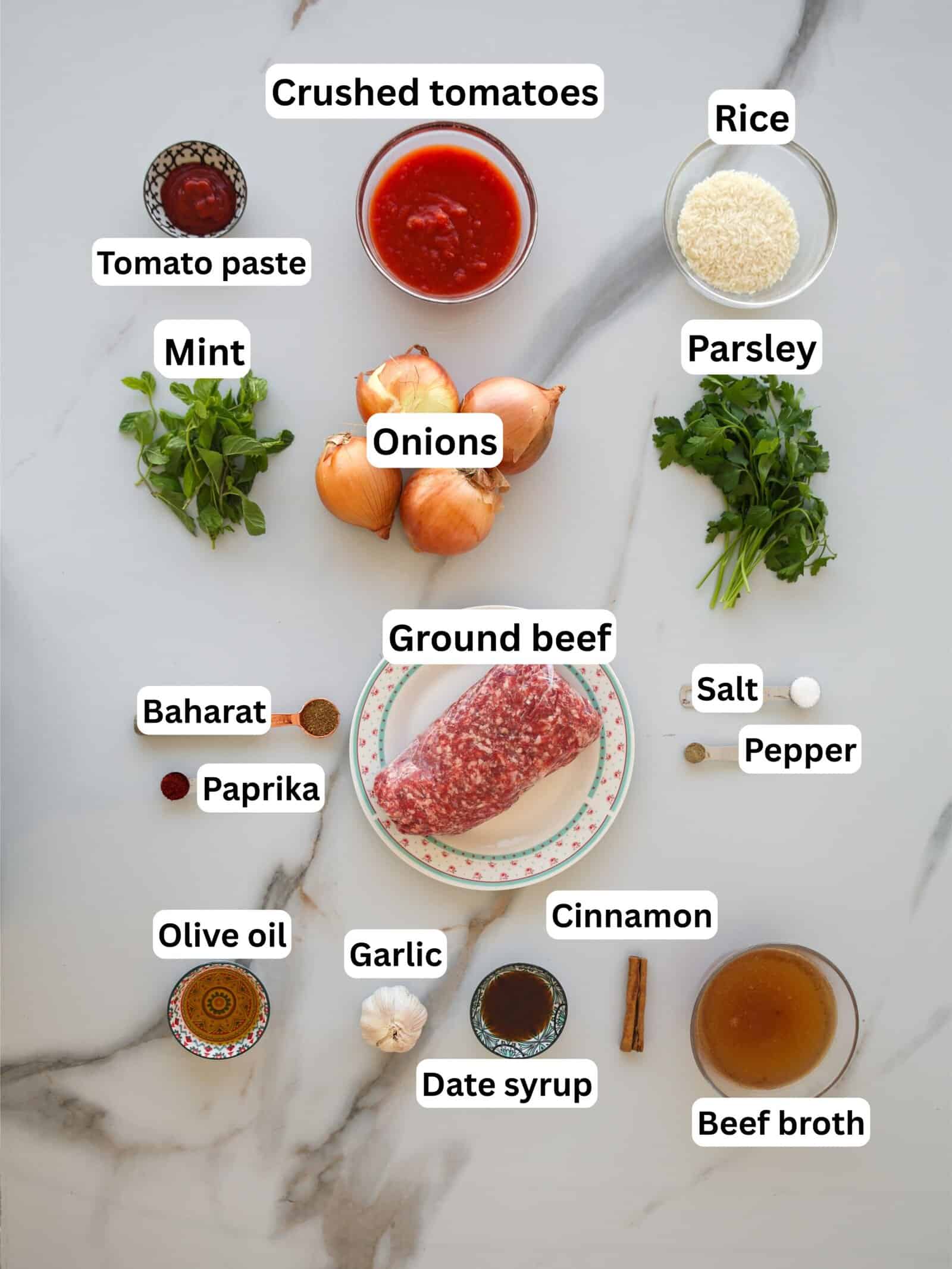 Top-down view of ingredients for a recipe, including ground beef, onions, garlic, rice, parsley, mint, crushed tomatoes, tomato paste, beef broth, olive oil, date syrup, spices (baharat, paprika, cinnamon), salt, and pepper.