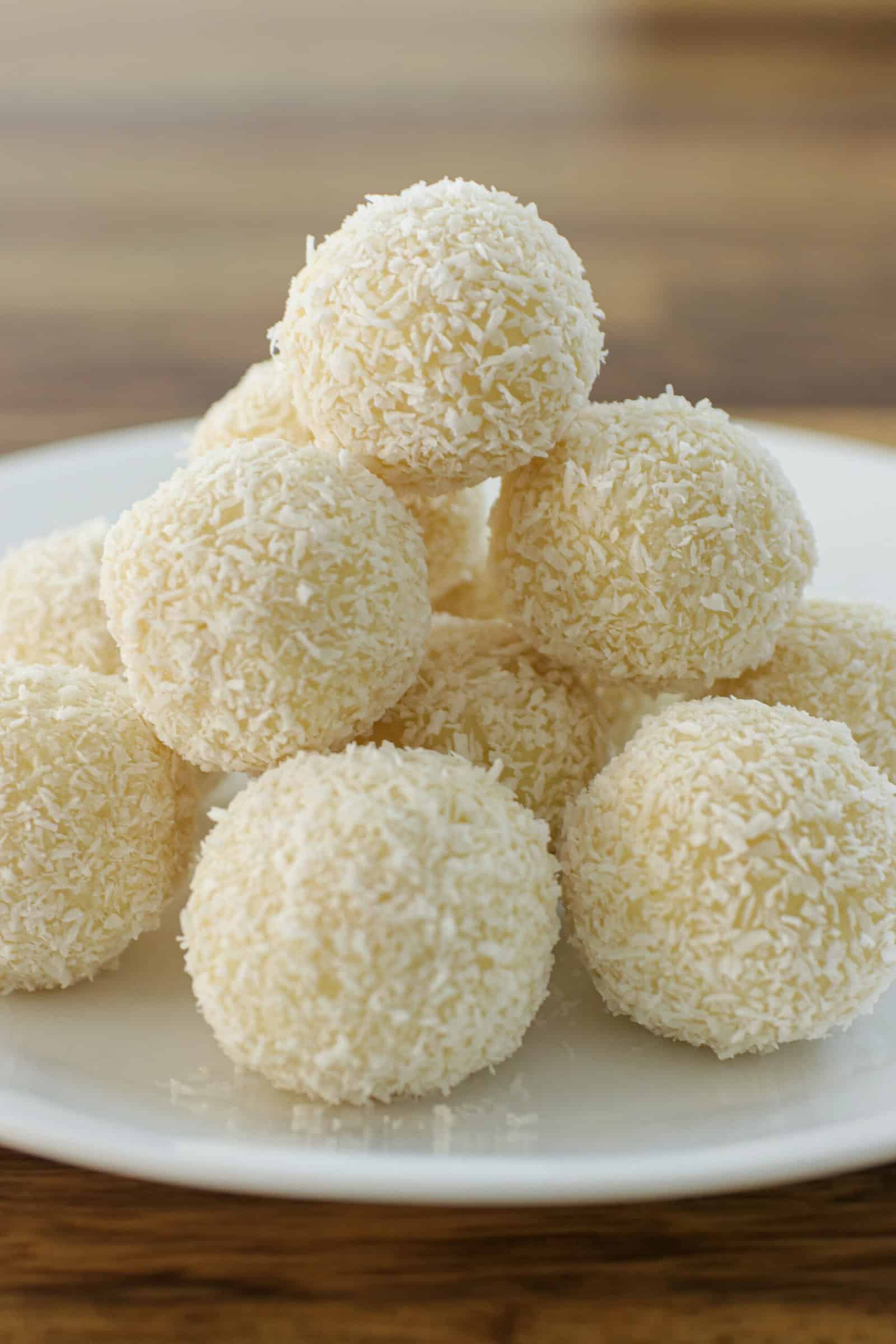 A white plate stacked with round, white coconut-covered dessert balls, set on a wooden surface.
