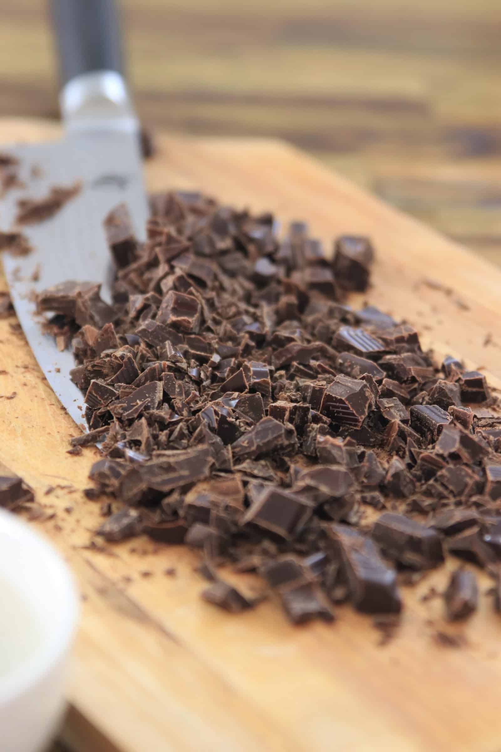 Chopped dark chocolate pieces on a wooden cutting board, with a knife beside them.