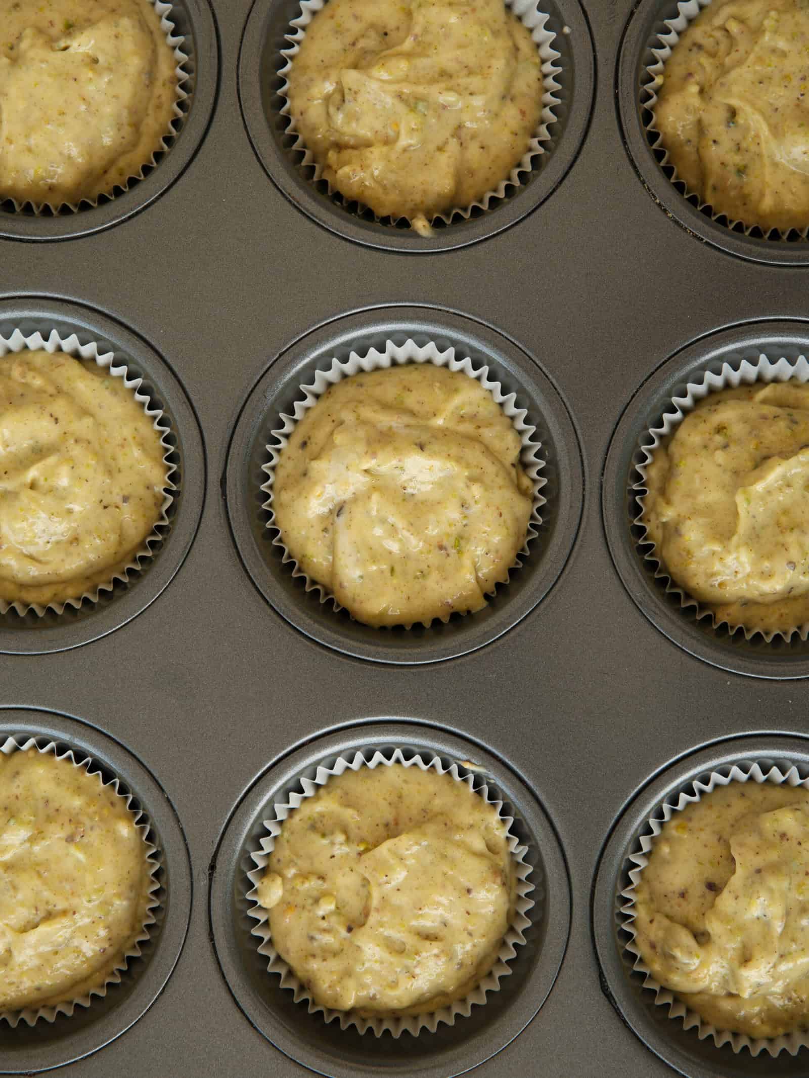 Close-up of a muffin tin filled with paper liners, each containing unbaked cupcake batter ready to be baked. The batter appears to have a slightly textured surface.
