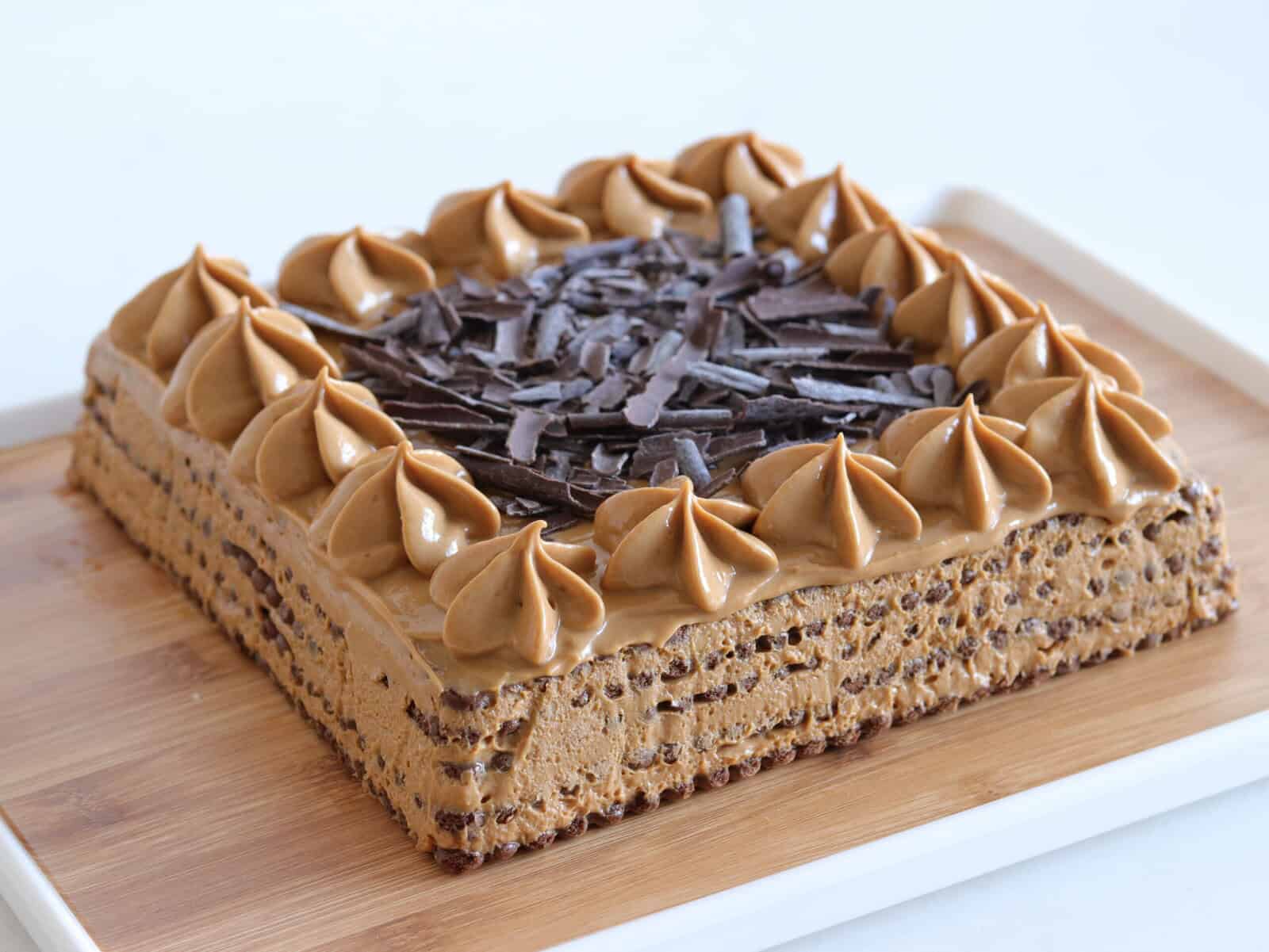 A square coffee-flavored chocotorta Argentina cake with piped frosting swirls on top, decorated with chocolate shavings in the center, served on a wooden tray.