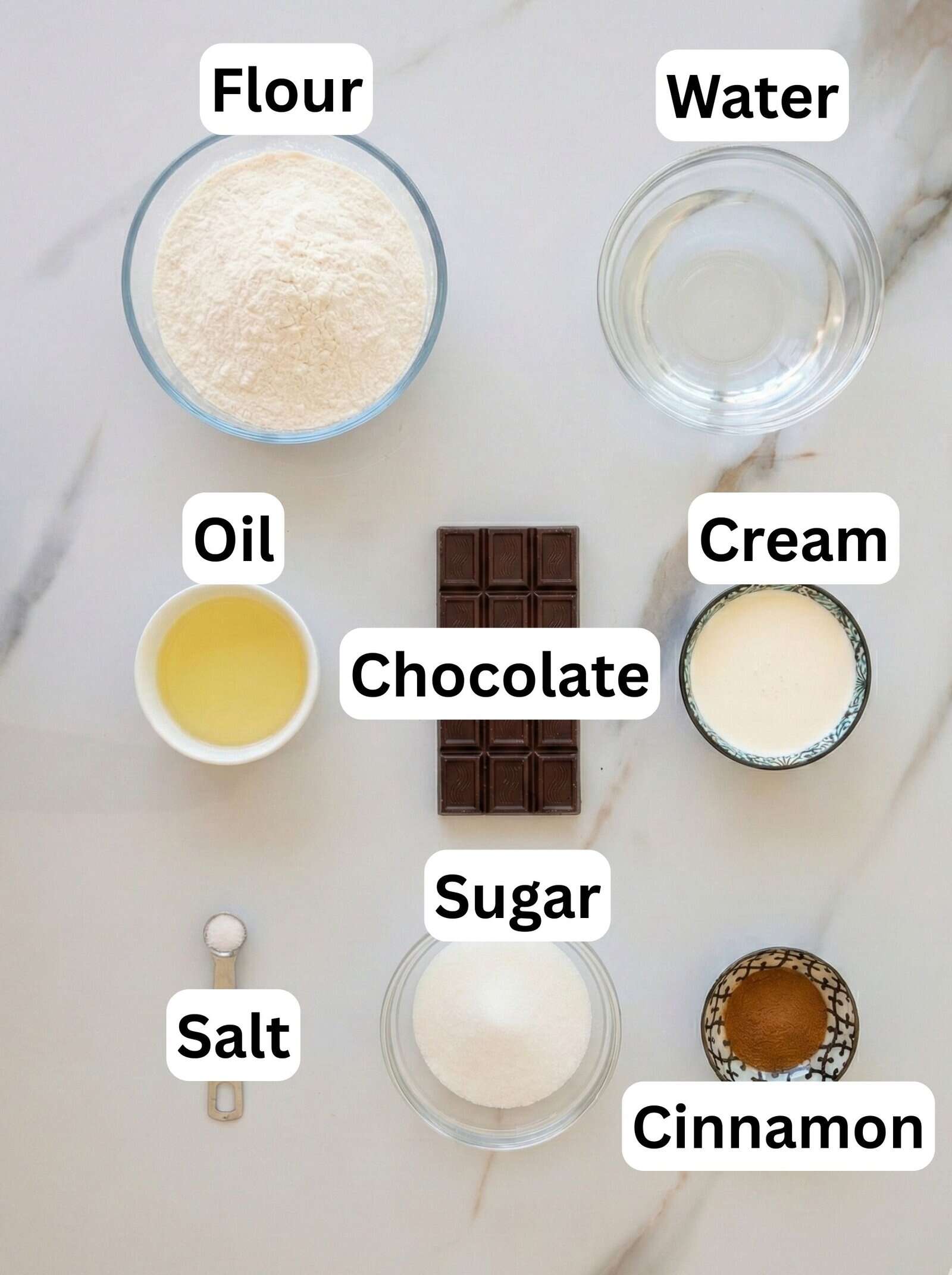 A top view of baking ingredients on a marble surface, labeled: flour, water, oil, chocolate, cream, sugar, salt, and cinnamon, each in separate bowls or containers.
