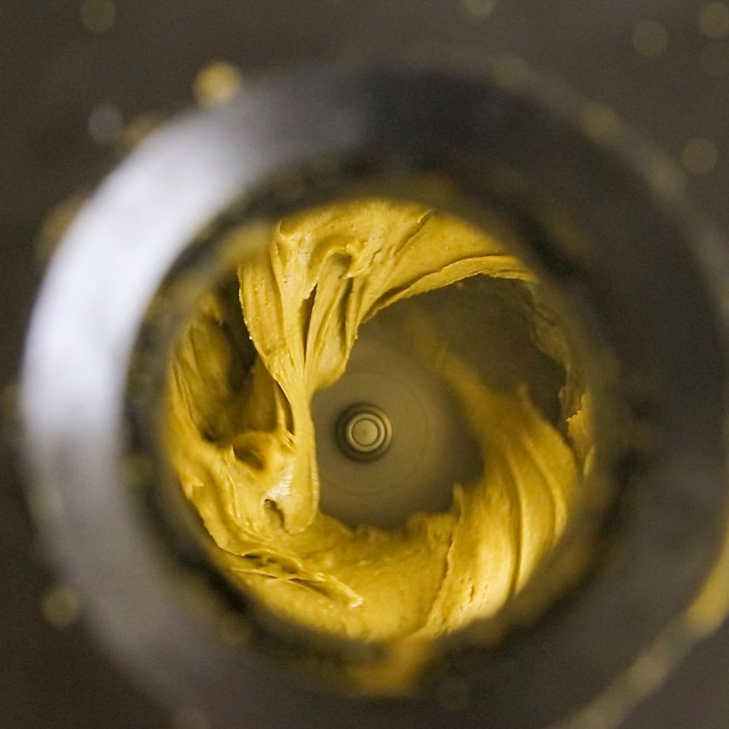 A view from above into a food processor, showing thick, creamy brown batter being mixed in a swirling motion around the central blade.