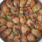 A round tray filled with baked stuffed onions, each browned on top and garnished with chopped fresh herbs. The onions are arranged closely together and appear moist and flavorful.