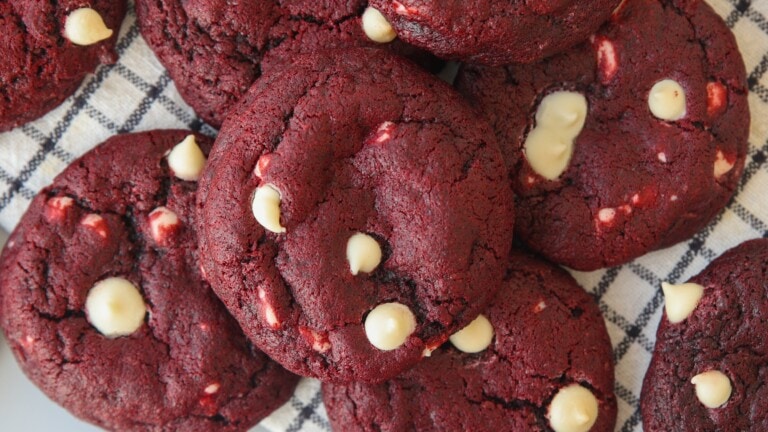 A close-up of several red velvet cookies with white chocolate chips, arranged on a black and white checkered cloth.