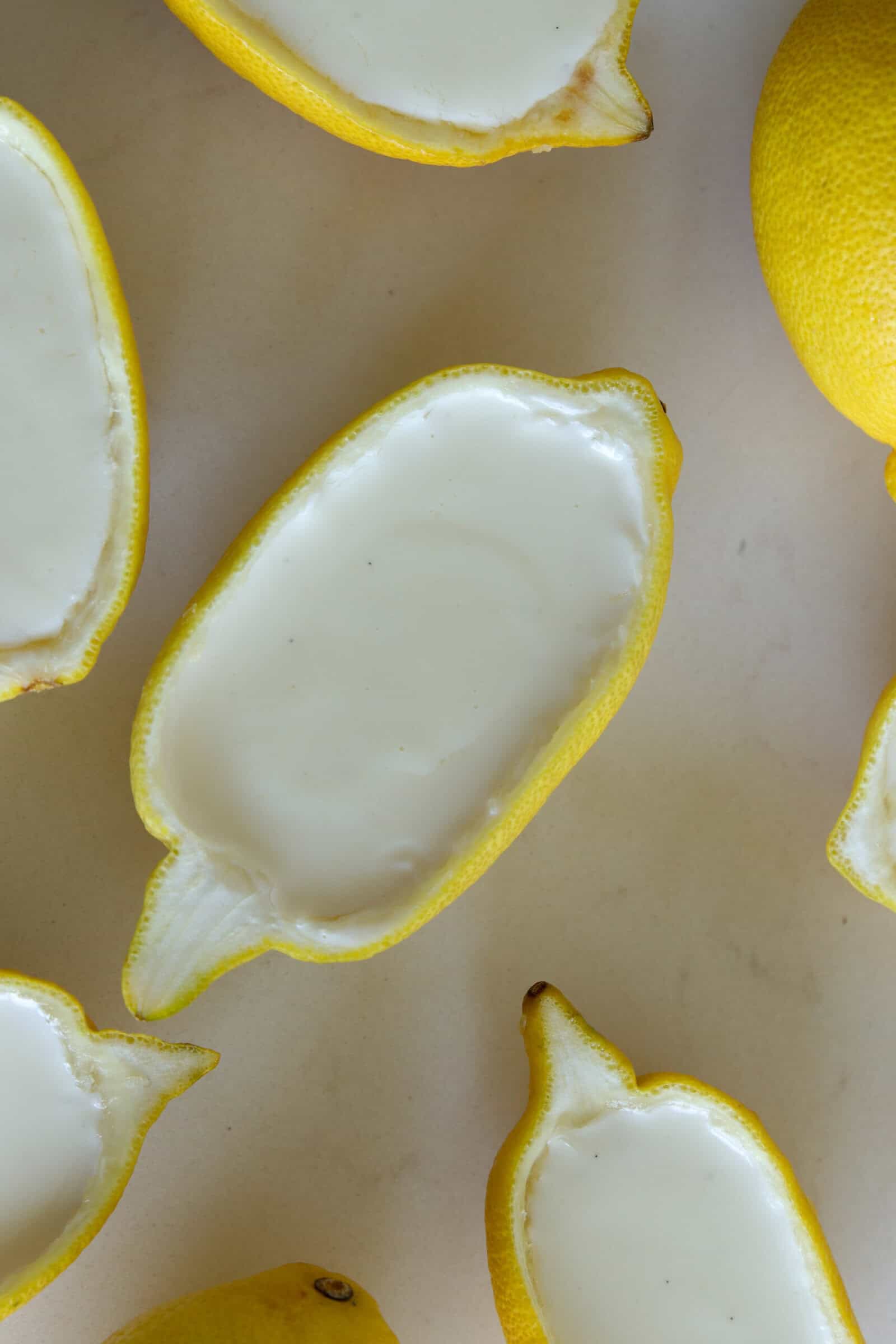 Halved lemons with the insides scooped out and filled with a smooth lemon posset, creamy white dessert, arranged on a light-colored surface.